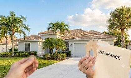 A hand holding a wooden house cutout and an "Insurance" folder in the foreground, with a sunlit, modern Florida home and palm trees in the background.